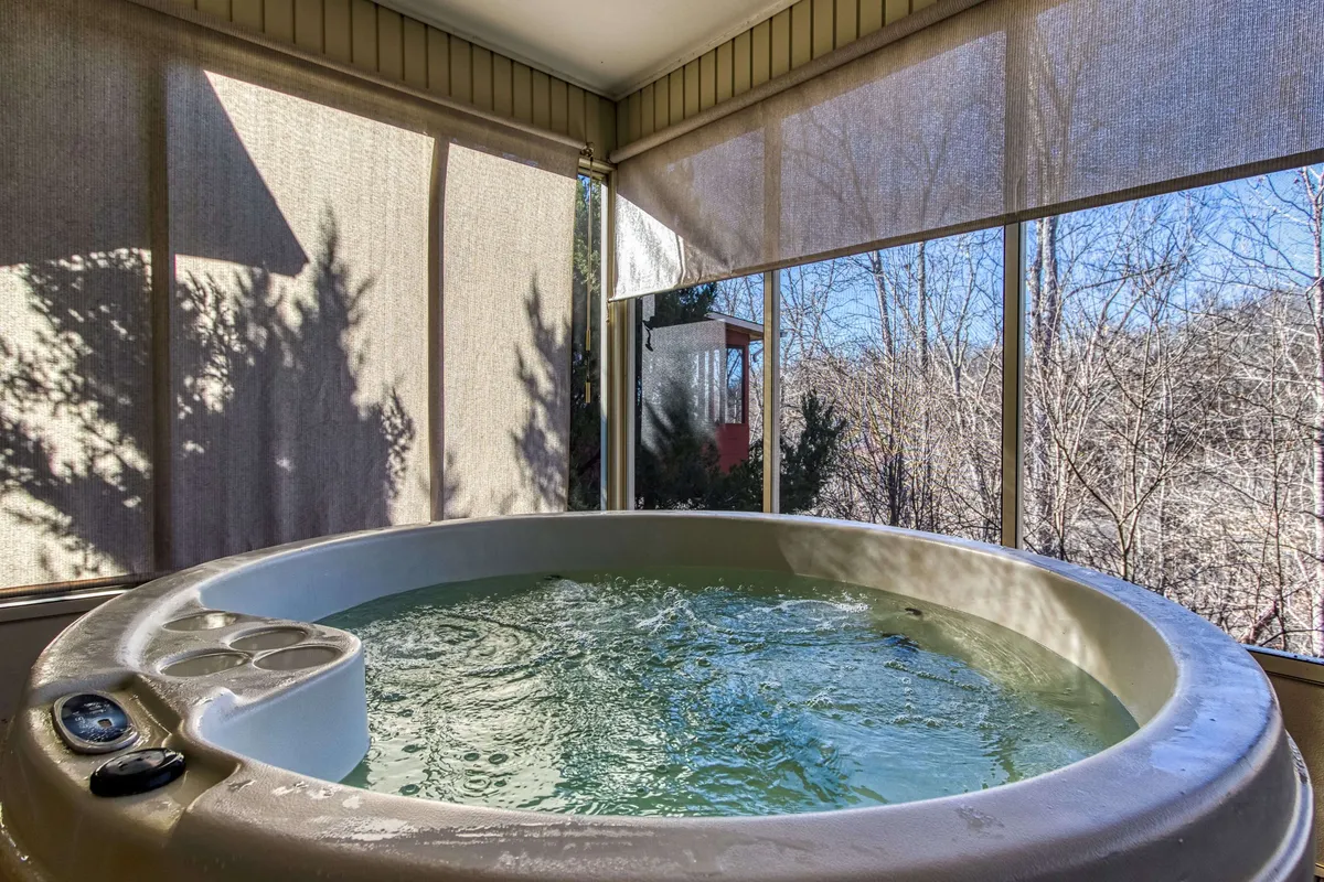 Inside, the private hot tub is bathed in natural light from large windows, offering a tranquil spot for relaxation with views outside. The space is perfect for unwinding together after exploring local attractions, capturing the social and restorative aspects of the retreat.