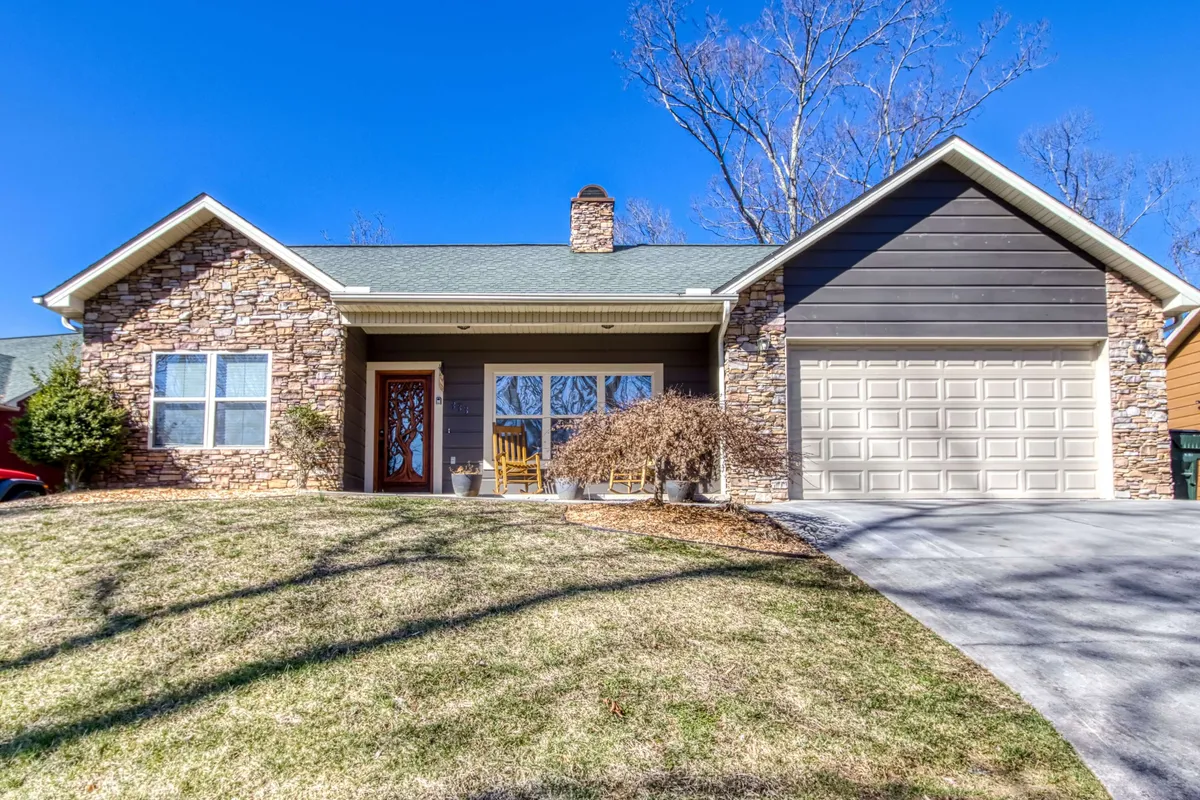 The image displays the inviting exterior of a single-family home with a charming stone facade, spacious front porch, and large windows that hint at a warm, welcoming interior. The porch overlooks sun-dappled trees, perfect for relaxing with family and enjoying beautiful sunrise or sunset views. Holiday decorations add a festive touch, evoking memories of special occasions and gatherings.