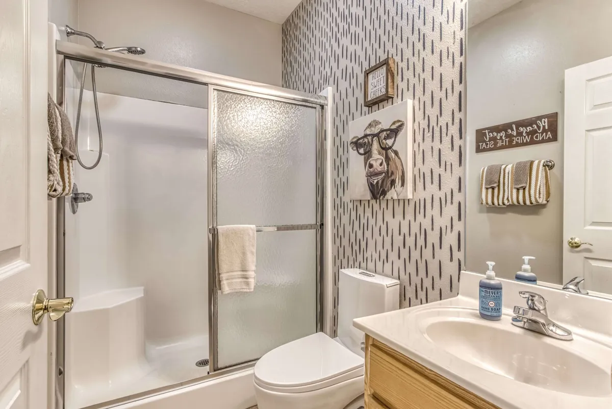 A bright and cheerful bathroom with a shower stall, cow-themed artwork, a vanity, and stylish bathroom accessories. The space is light-hearted and functional, suitable for busy mornings or relaxing after adventures.