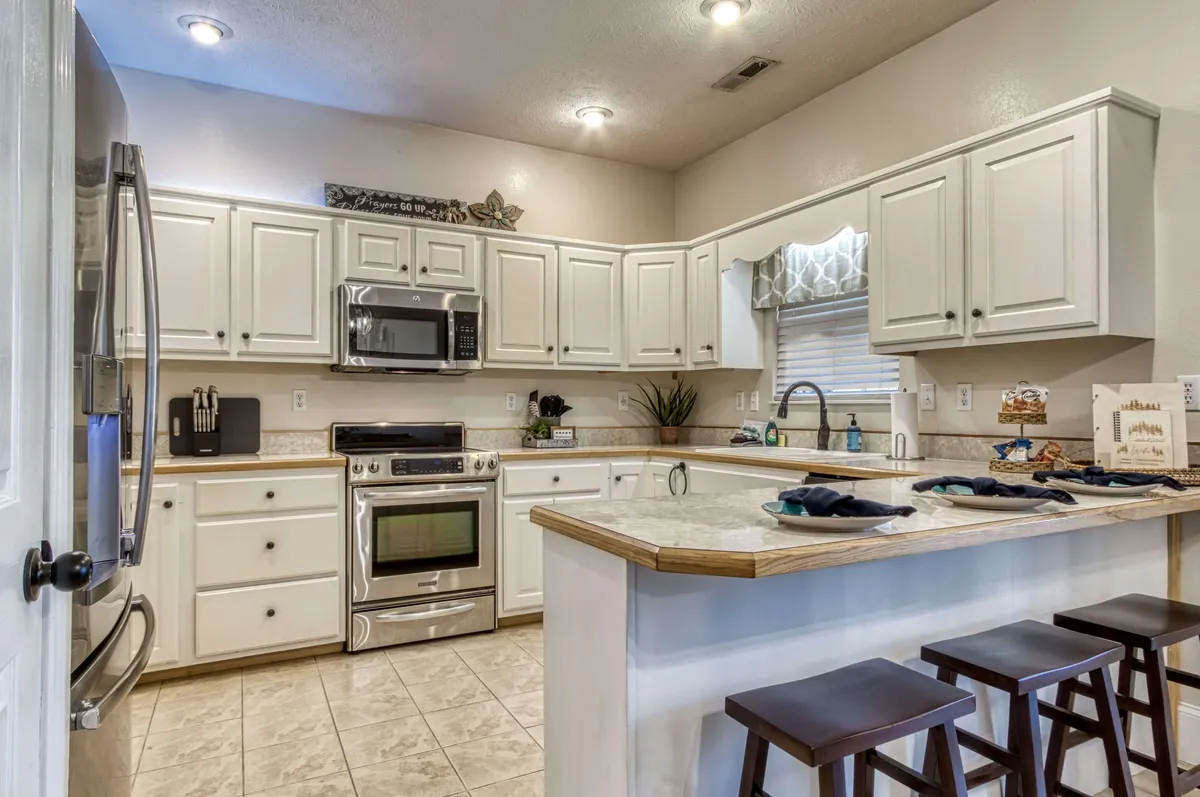 A well-lit, fully equipped kitchen with stainless steel appliances, a granite countertop, a kitchen island with bar seating, and a window that floods the space with natural light. The island allows for both meal prep and casual conversation, emphasizing the kitchen’s utility and openness.
