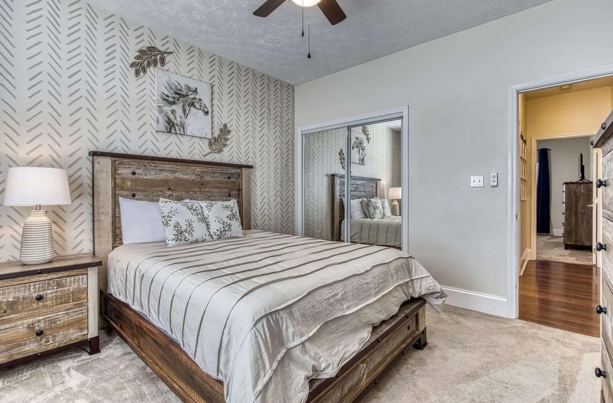A rustic wooden bed is the centerpiece, enhanced by decorative wall art, a nightstand with a lamp, and a mirrored closet. The space feels serene and inviting, ideal for unwinding after a busy day.