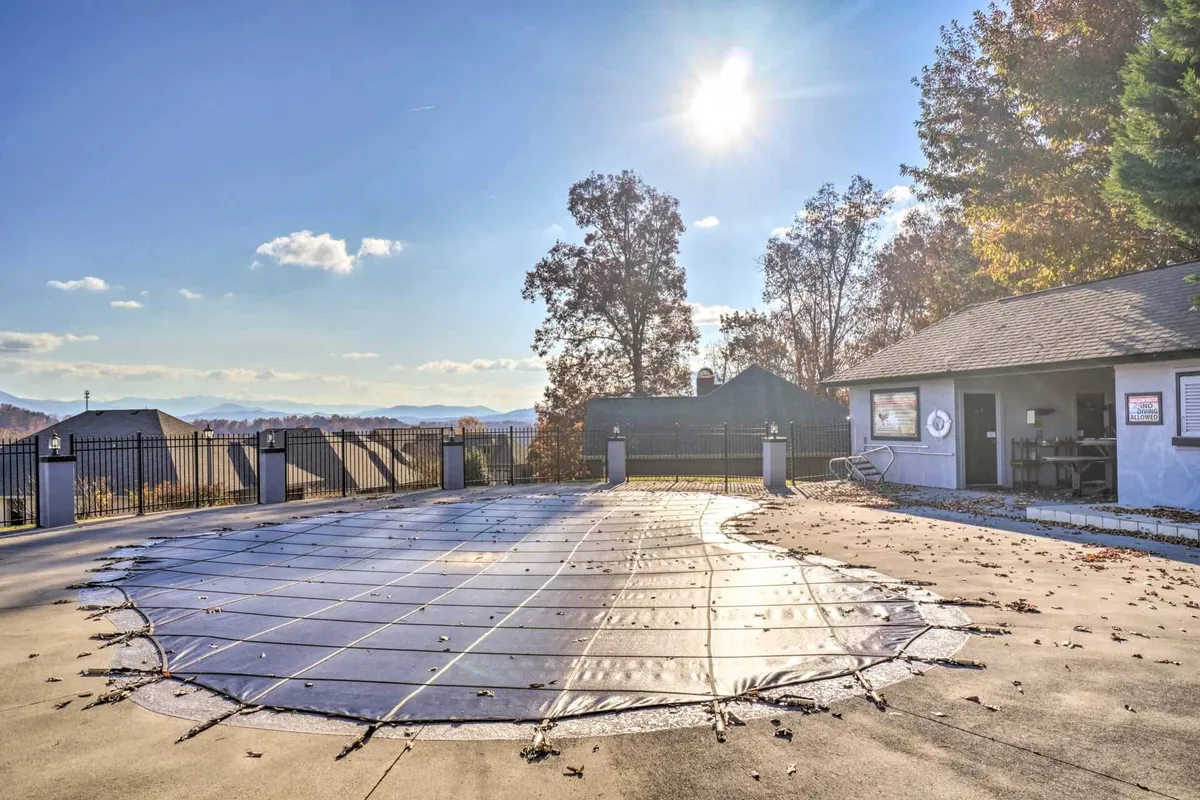 An exterior shot of the seasonal community swimming pool, surrounded by trees and set against a backdrop of stunning mountain views. The pool cover is visible, emphasizing its seasonal availability.