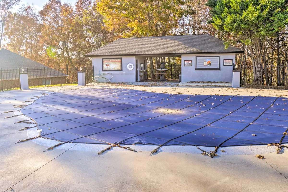 A tranquil community pool with a cover, pavilion, and surrounding trees, offering a peaceful spot for family relaxation and play during warmer months. The image evokes sunny afternoons and togetherness in a natural setting.