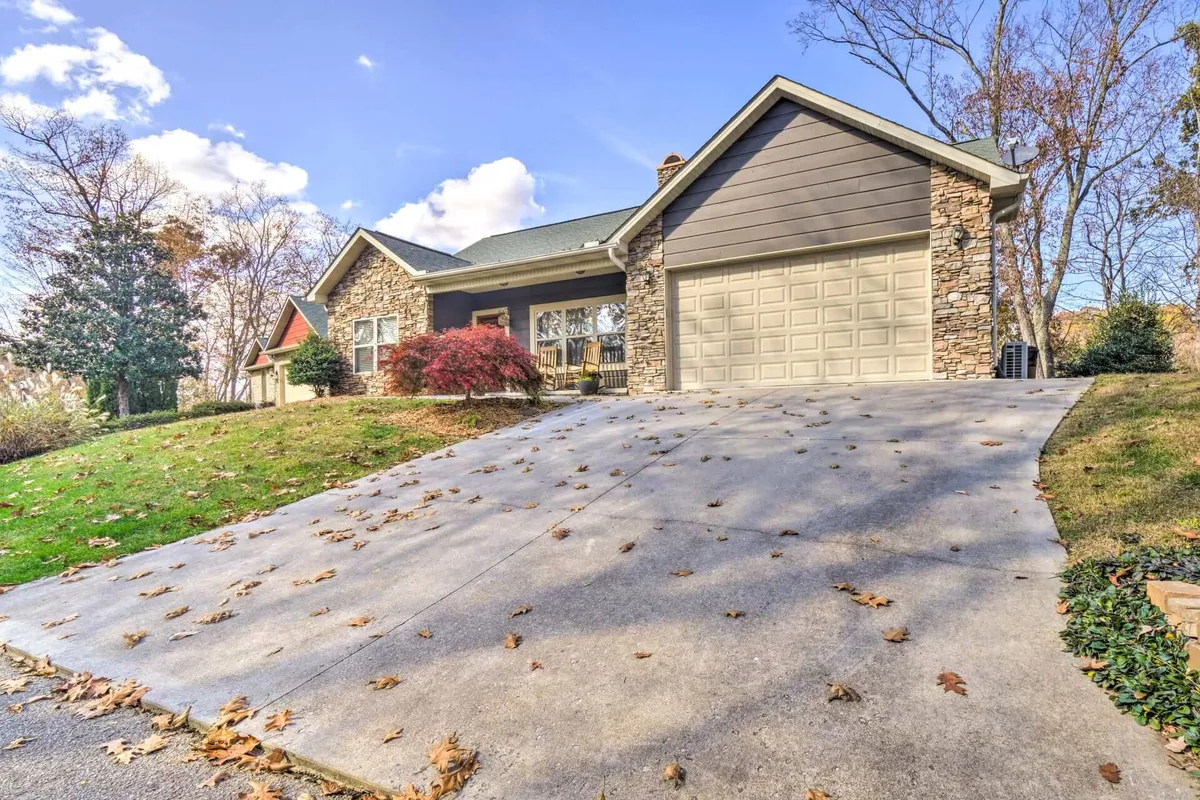 The stone facade of Saddleback Retreat framed by a lush green lawn, driveway, and a striking red shrub. The welcoming exterior sets the stage for family gatherings and outdoor entertaining after a day of exploration.
