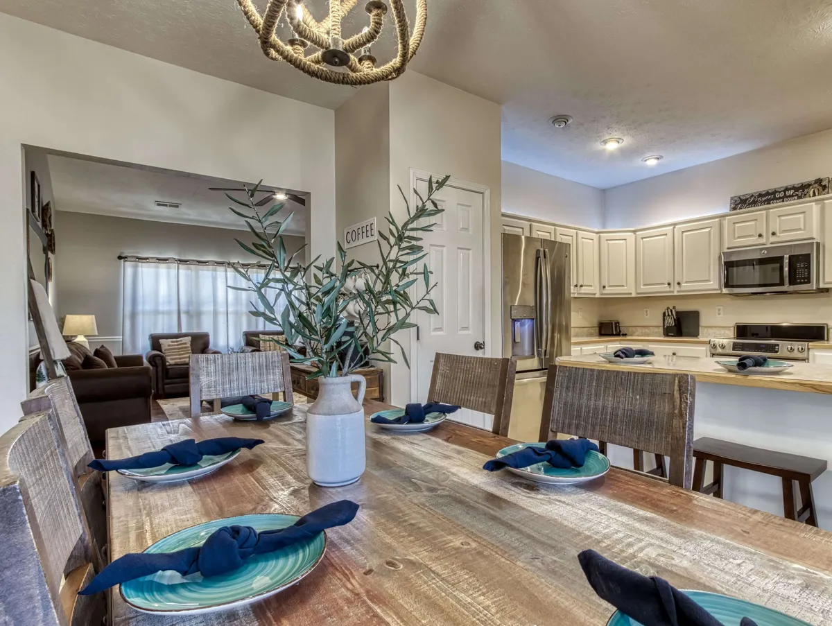 This image presents a dining table set under a chandelier, with a clear view into the adjacent kitchen entrance. The centerpiece of greenery and inviting decor hint at intimate meals and festive gatherings, matching the mood of shared feasts and togetherness.